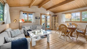 A cozy cabin interior with a sofa, coffee table, dining table, and chairs. - Cozy home in Bogø By with WiFi (Bogø By)
