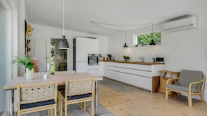 Een moderne keuken met witte kastjes, een houten eettafel met stoelen, een hanglamp en een raam met uitzicht op groen.