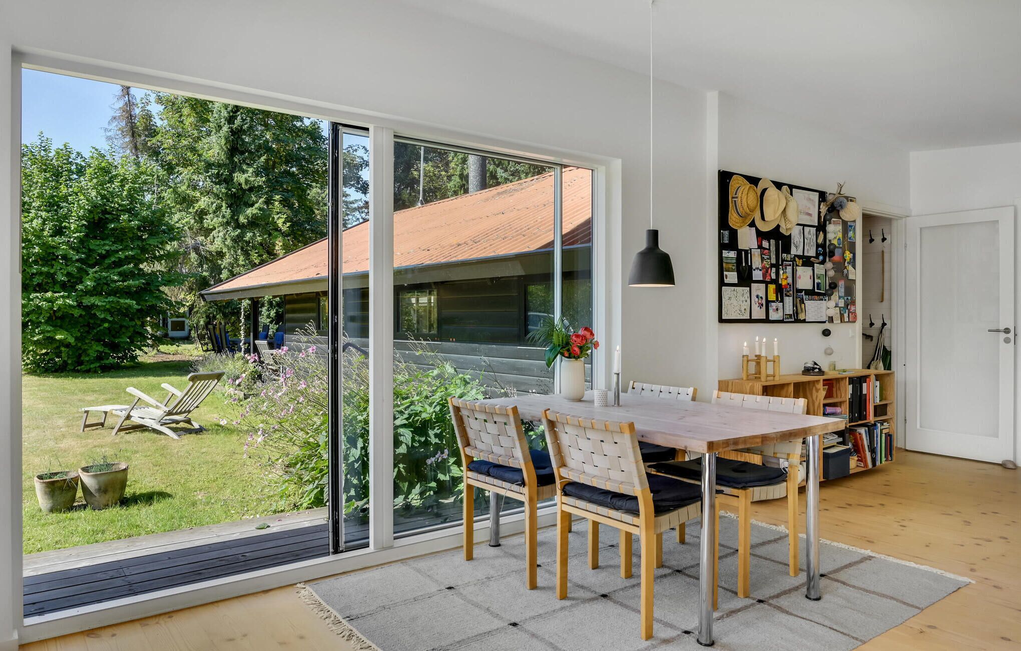Un intérieur moderne comprenant un coin repas, de grandes portes-fenêtres coulissantes donnant sur un jardin et un mur décoré de divers objets.