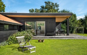 Una casa moderna con facciata in legno, un ingresso con porta in vetro, un patio con tavolo e sedie, e un prato.