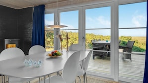En matplats med ett bord dukat för sex personer, en vas med torkade växter och utsikt över en vingård genom stora glasdörrar.