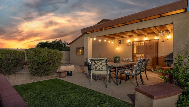 Un patio con mesa y sillas, una parrilla y luces colgantes.