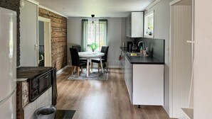 Cocina compacta con comedor, estufa, lavamanos y ventana con cortinas.