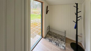 Un pasillo con piso de madera, un banco, un perchero y una puerta que da al exterior.
