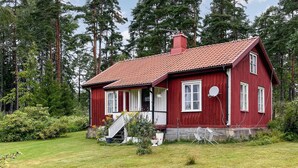 Una casa de madera roja con techo de tejas, rodeada por un patio cubierto de césped y un bosque denso.