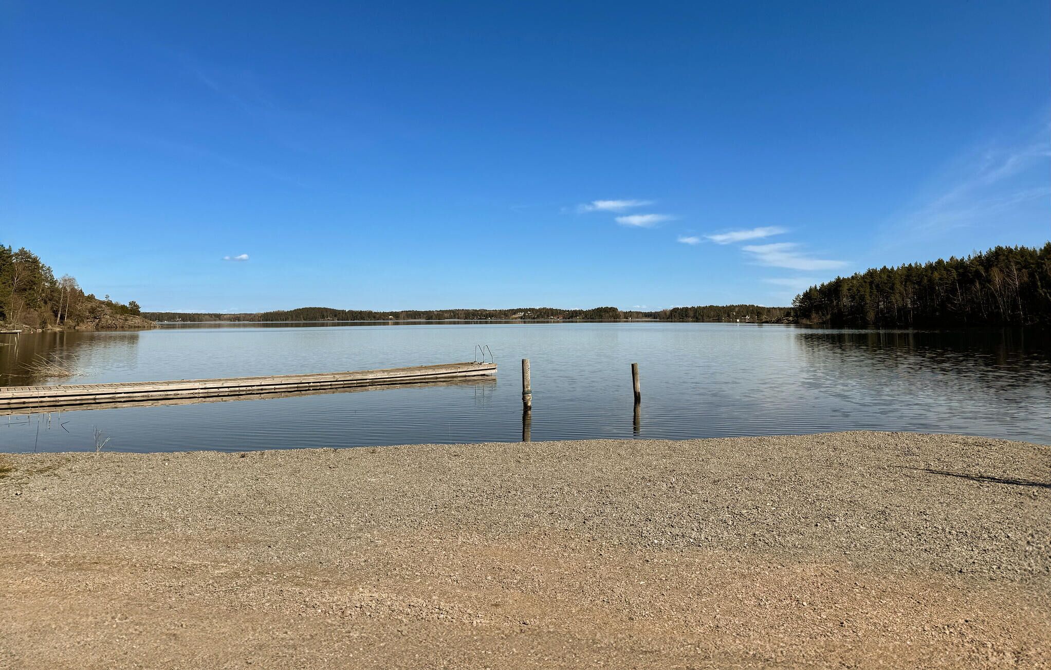 En stilla sjö med en träbrygga som sträcker sig ut i vattnet, omgiven av en skogbeklädd strand.