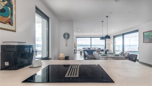 Eine moderne Küche mit eingebautem Herd, ein Essbereich mit Meerblick und ein Wohnzimmer mit Sofa und Couchtisch.