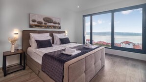 Ein modernes Schlafzimmer mit einem großen Bett, einem Nachttisch, einer Wandleuchte und Meerblick.