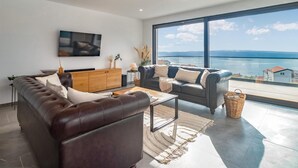 Ein modernes Wohnzimmer mit großem Fenster, einer Ledersofa, einem Holzschrank und einem Flachbildfernseher.