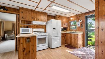 A modern kitchen with wooden paneling, a white refrigerator, a stove, and a microwave.