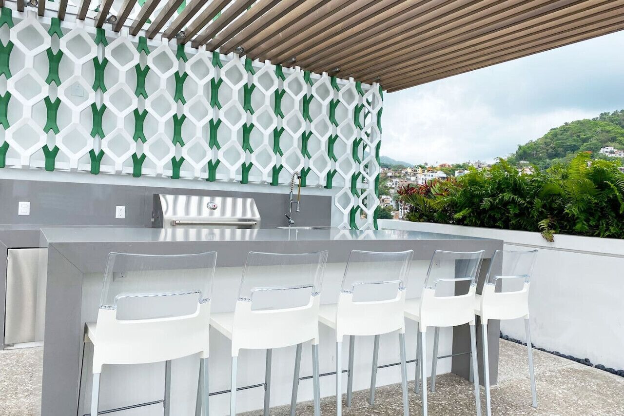 Un área de cocina al aire libre con barra integrada y cuatro sillas blancas.