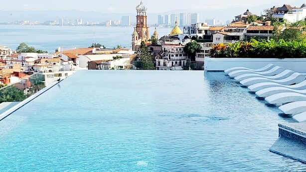Una piscina infinita larga y despejada, con un paisaje urbano y una iglesia destacada al fondo.