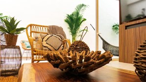 Una mesa de comedor de madera con un centro de mesa tejido, sillas de mimbre y plantas en macetas.