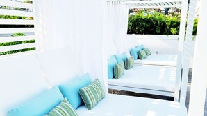 Un espacio de estar exterior con asientos blancos, cojines a rayas, una pérgola y vistas a zonas verdes.