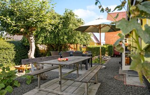 Enjoy dining or socializing in this charming outdoor space surrounded by lush greenery and a large umbrella.