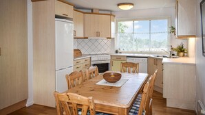 A compact kitchen with wooden cabinets, a built-in oven, a dishwasher, and a dining table with chairs.