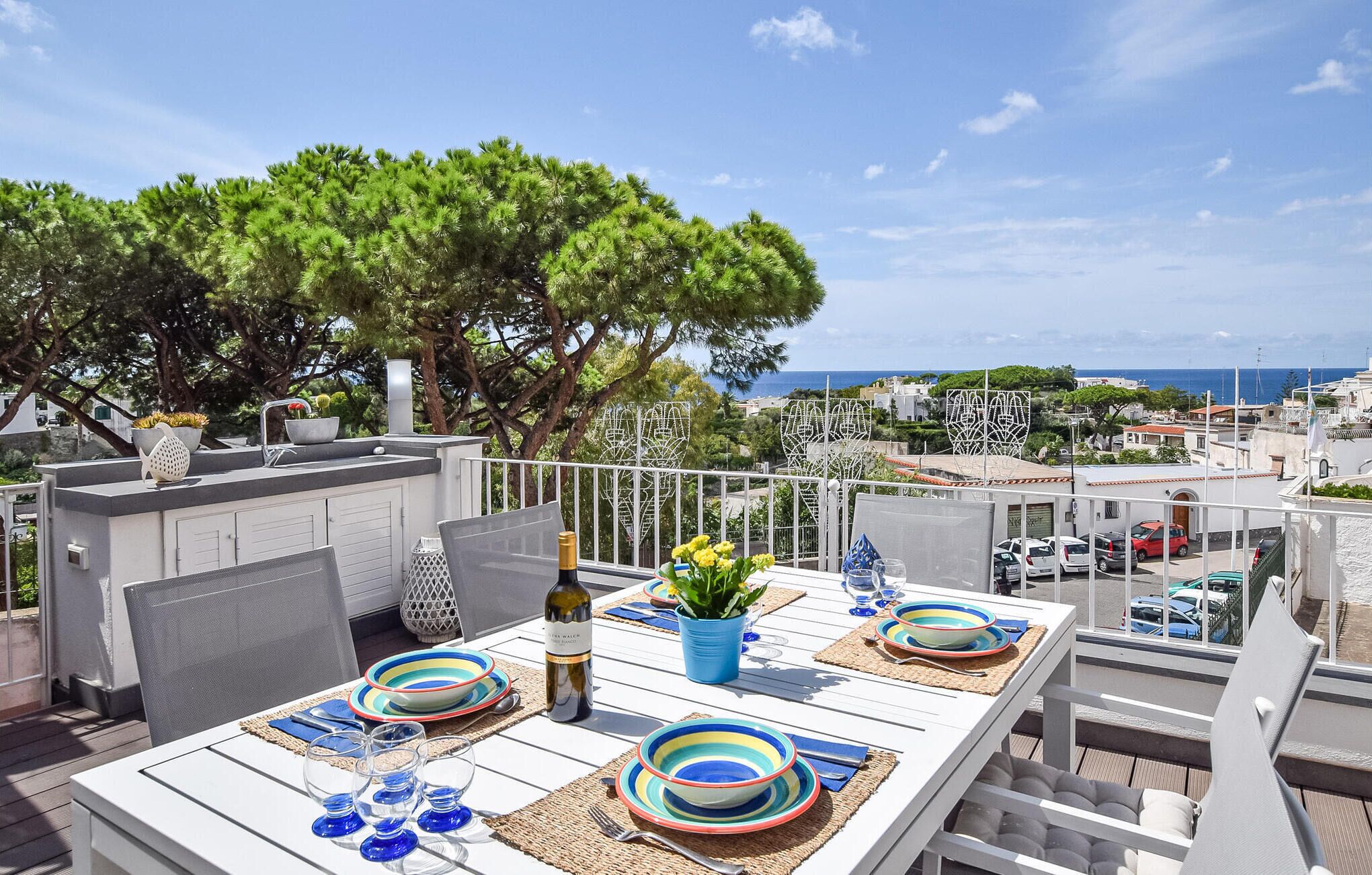 A rooftop terrace with a table set for dining, overlooking a coastal town.