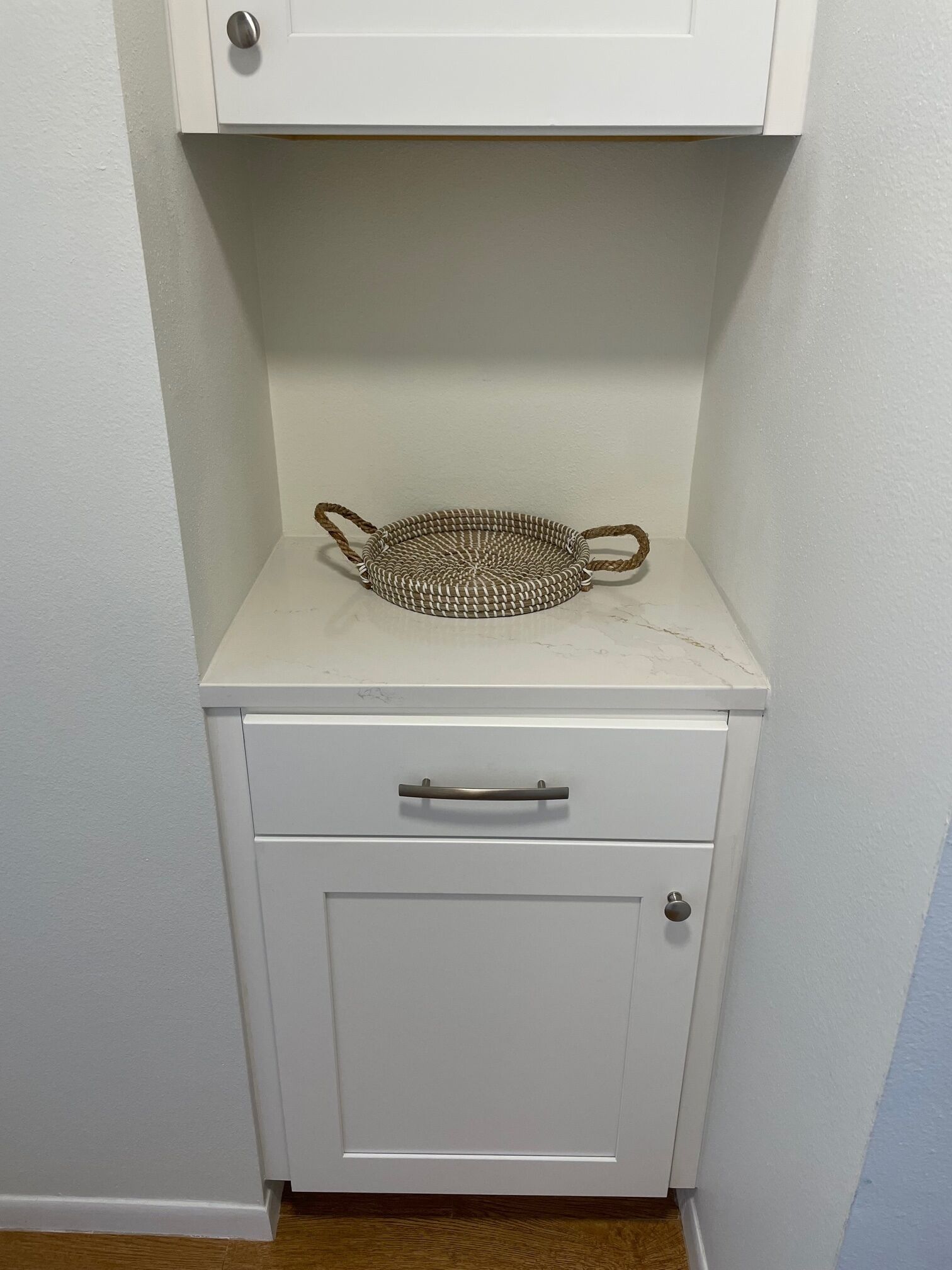 A white cabinet with a woven basket on top and a drawer below.