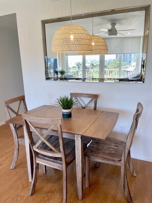 Ein Essbereich mit Holztisch und -stühlen, einer hängenden Lampenschirm aus Bändern und Blick ins Freie durch ein großes Fenster.