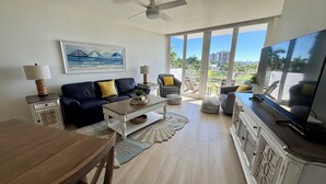 A spacious living room with a large TV, a ceiling fan, and a view of the outdoors. - Hello Sunshine!  Eat. Sleep. Beach. Repeat. (Marco Island)
