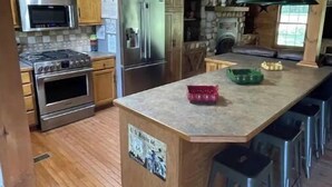 Une cuisine avec des meubles en bois, un réfrigérateur en acier inoxydable, un four à micro-ondes, un four traditionnel et un coin bar avec des tabourets.