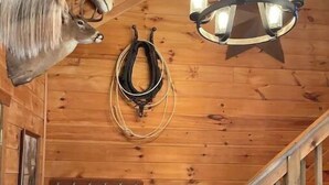 L’intérieur d’un chalet en bois, avec une tête d’animal fixée au mur, un lustre et une corde enroulée accrochée au mur.