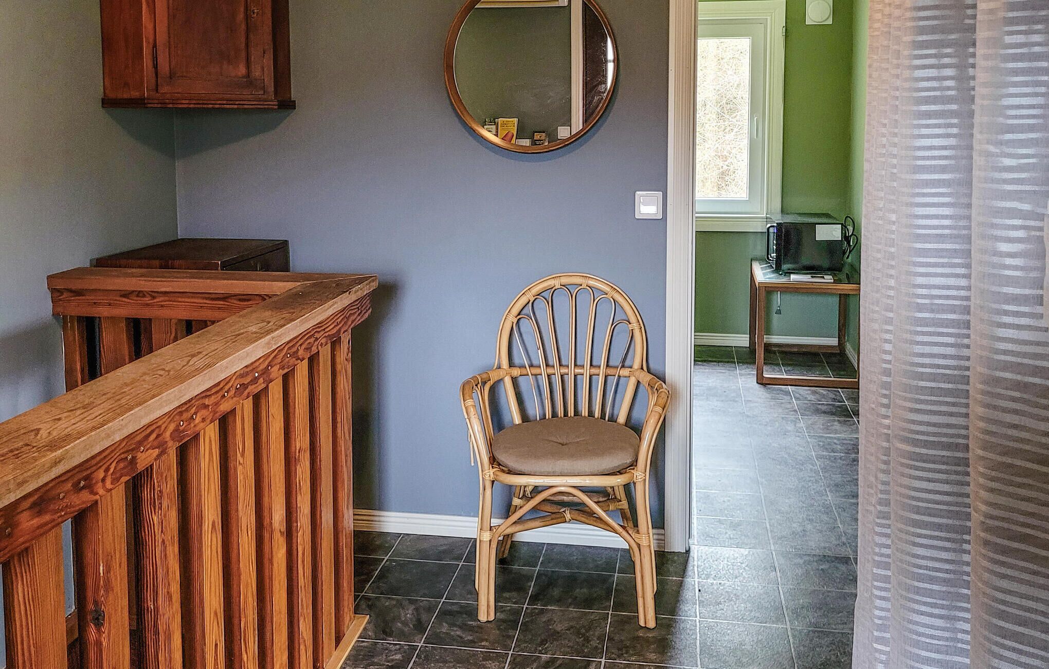 A wooden bench, a wicker chair, a mirror, and a small table with a television in a room with green walls and tiled flooring.