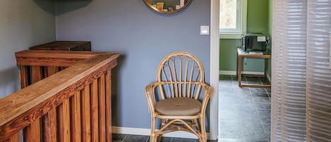 A wooden bench, a wicker chair, a mirror, and a small table with a television in a room with green walls and tiled flooring.