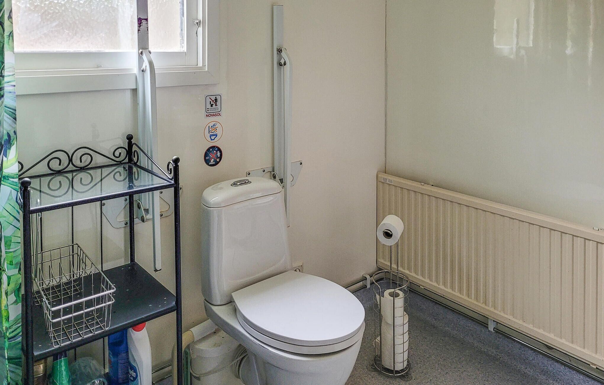 A small, compact bathroom with a toilet, a shelf with cleaning supplies, and a radiator.