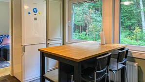 A compact kitchen with a wooden table and chairs, a white refrigerator, and a window with a view of greenery. - Lovely home in Hishult with WiFi (Hishult)