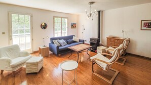 Een ruime woonkamer met een blauwe bank, witte fauteuils, een ronde salontafel en een houten kast.