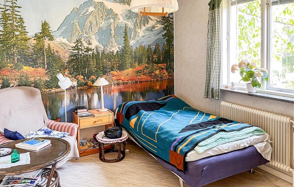 A cozy bedroom with a bed, a chair, a small table, and a window with a view of trees and mountains.
