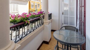 A balcony with a round table and wicker chairs, a white door, and a view of colorful buildings. - Estúdio - Zona Histórica de Pombal (Pombal)
