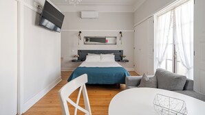 A modern bedroom with a bed, a TV mounted on the wall, a chandelier, and a window with curtains. - Estúdio - Zona Histórica de Pombal (Pombal)