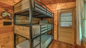 Uma cama de solteiro em um quarto de cabana de madeira, com porta e janela com persianas.