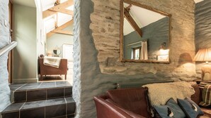 A rustic interior with stone walls, a leather sofa, and a staircase leading to another room. - A quirky converted barn. (Cardigan)