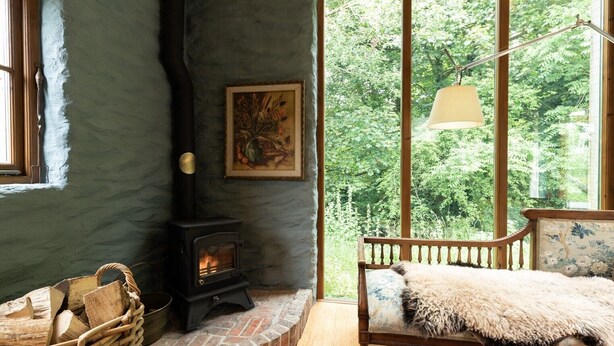 A cozy room with a stone fireplace, a wooden bench with a fur throw, and a large window overlooking greenery. - A quirky converted barn. (Cardigan)