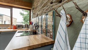 A modern kitchen with a wooden countertop, a stone wall, and a view of the outside. - A quirky converted barn. (Cardigan)