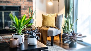 Una sala de estar acogedora con chimenea de ladrillo, un sillón cómodo y diversas plantas en macetas.
