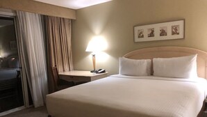 Habitación de hotel con una cama grande, un escritorio con lámpara, una silla y una puerta corrediza.