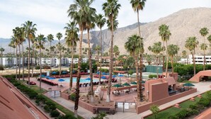 Un resort con piscina, palmeras y montañas al fondo.