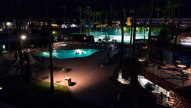 Vista nocturna de un resort con piscina, sillas de descanso y palmeras.