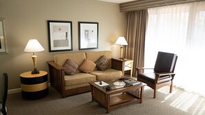Habitación de hotel con sofá, dos mesitas de noche con lámparas, una mesa de centro, televisor y alfombra estampada.