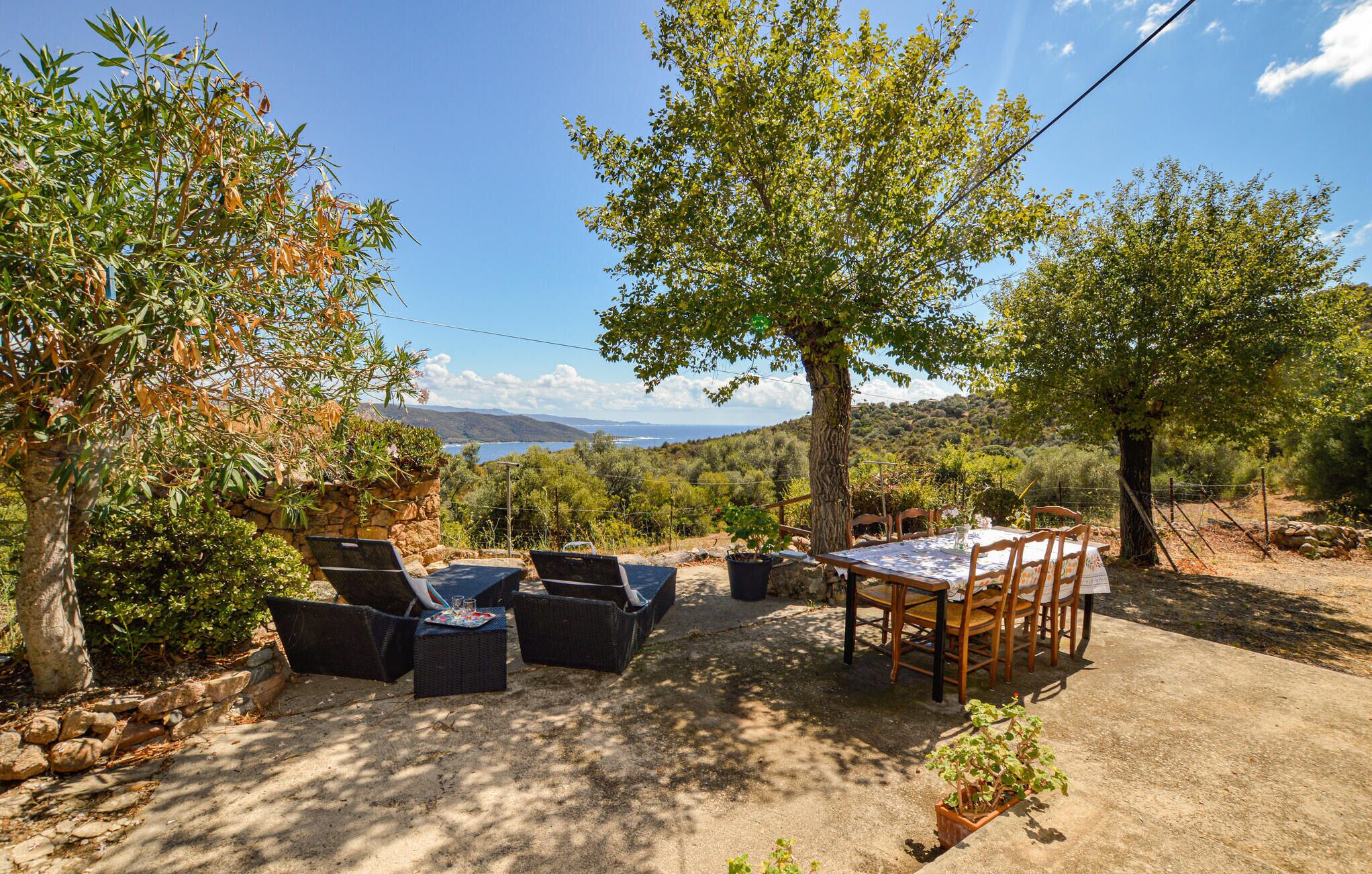 An outdoor dining area with a table and chairs, surrounded by trees and a view of the landscape.