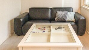 A living room with a black leather sofa, a glass-top coffee table with various items, and a window to the right. - 4 bedroom cozy home in Brottby (Brottby)