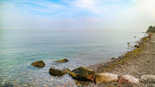 Ein freier Blick auf einen Kiesstrand mit ruhigem Wasser und einer entfernten Küste.