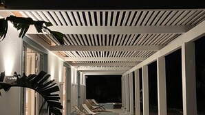Een overdekt buitengebied met lounge stoelen en een rond tapijt.