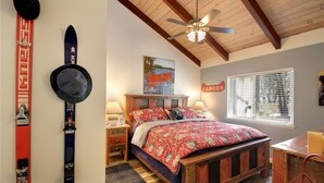 Ein Schlafzimmer mit einem hölzernen Bett, einem Deckenventilator, einem Fenster mit Jalousien und Ski sowie einem Hut, der an der Wand hängt.