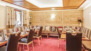 Ein Restaurant mit Holzwandverkleidung, einem roten Teppich mit Muster und verschiedenen Tischgestaltungen.