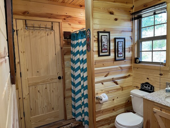 Une salle de bain rustique, aménagée dans une cabane en bois, avec une douche, des toilettes et un lavabo.